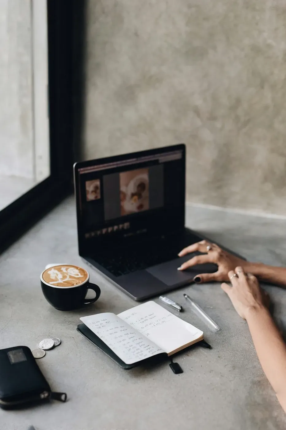 Editing photos at a laptop with a latte and notebook